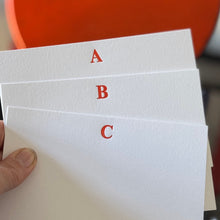 Hand holding three white cards labeled A, B, and C with a blurred red circular object in the background.