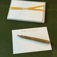 A solid brass fountain pen with a set of white notecards with the text Save The Date printed in Gold ink