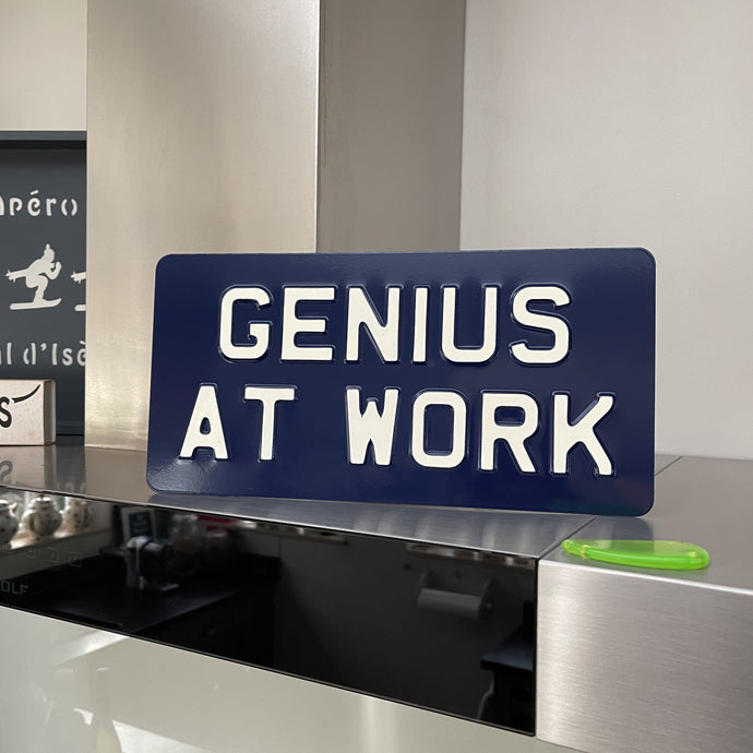 GENIUS AT WORK metal sign Light Cream text on Navy Blue background 