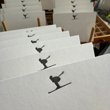 White postcards with dark grey silhouette of a skier shussing in a tuck position
