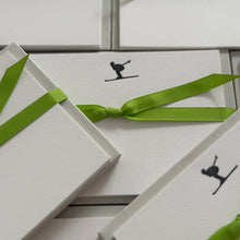 Multiple sets of notecards featuring a skier in a tucked position with a green ribbon tied around the cards
