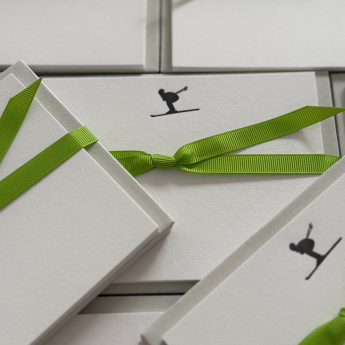 Multiple sets of notecards featuring a skier in a tucked position with a green ribbon tied around the cards
