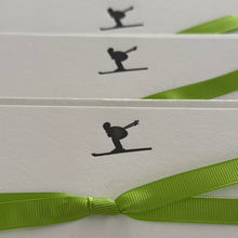 Multiple sets of notecards featuring a skier in a tucked position in dark grey with a green ribbon tied around the cards
